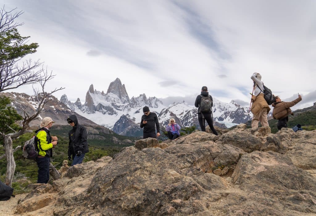 Several people standing on a rock overlooking the jagged Mountain View of Fitz Roy.