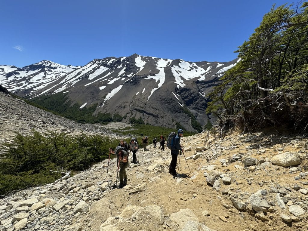 Hikers hiking down a scraggly rock-covered mountain, leaning on their hiking poles.