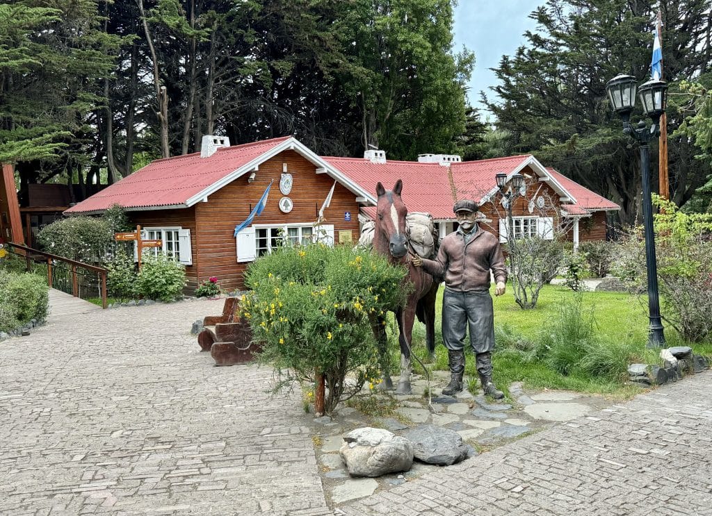 A small park with a statue of a man leading a horse in front of a small cabin.