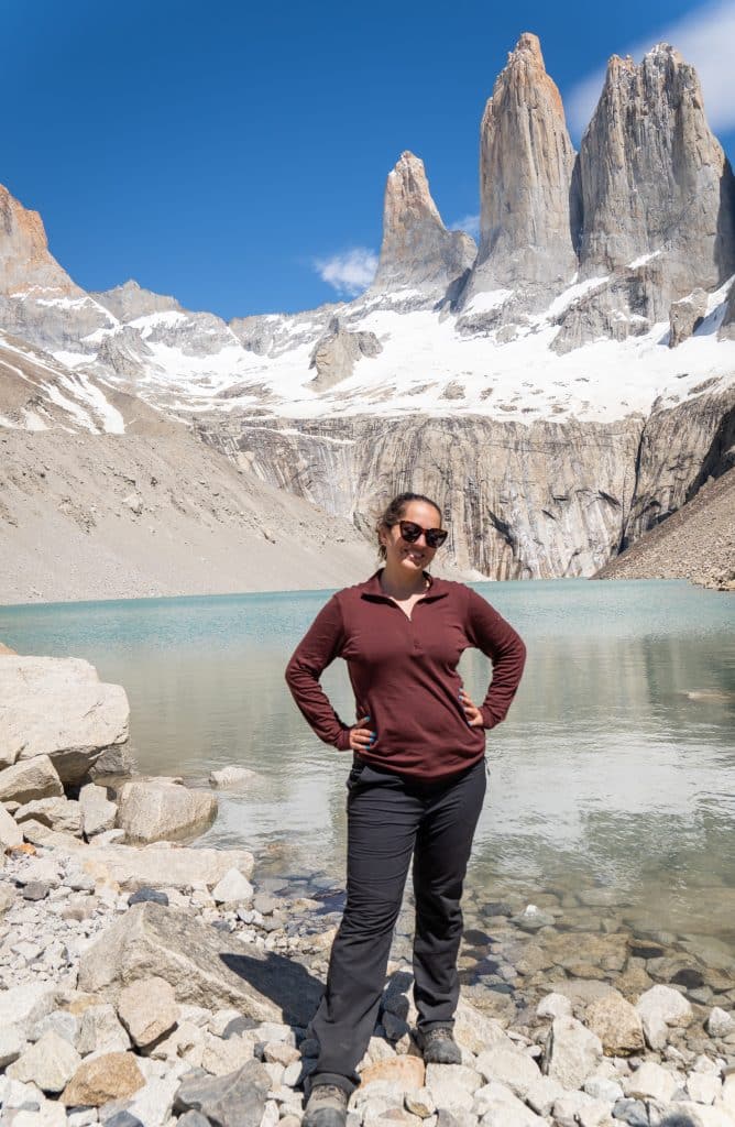 Kate standing with her hands on her hips in front of the pale turquoise lake at the base of the towers.