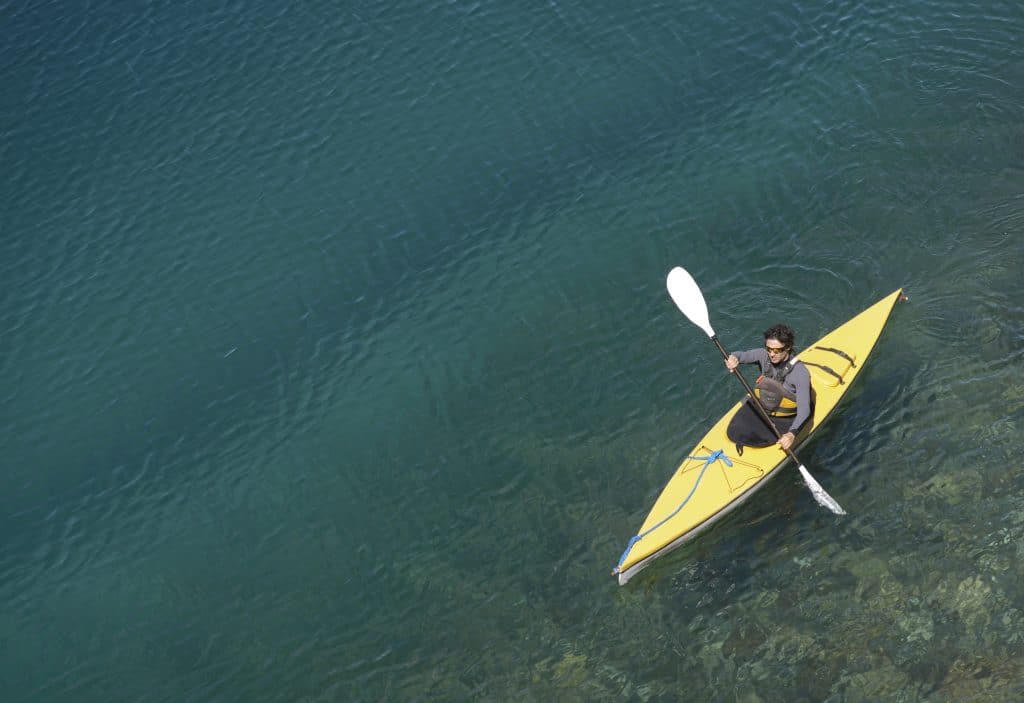 A lone kayaker in a yellow kayak on a blue-green lake in Patagonia.