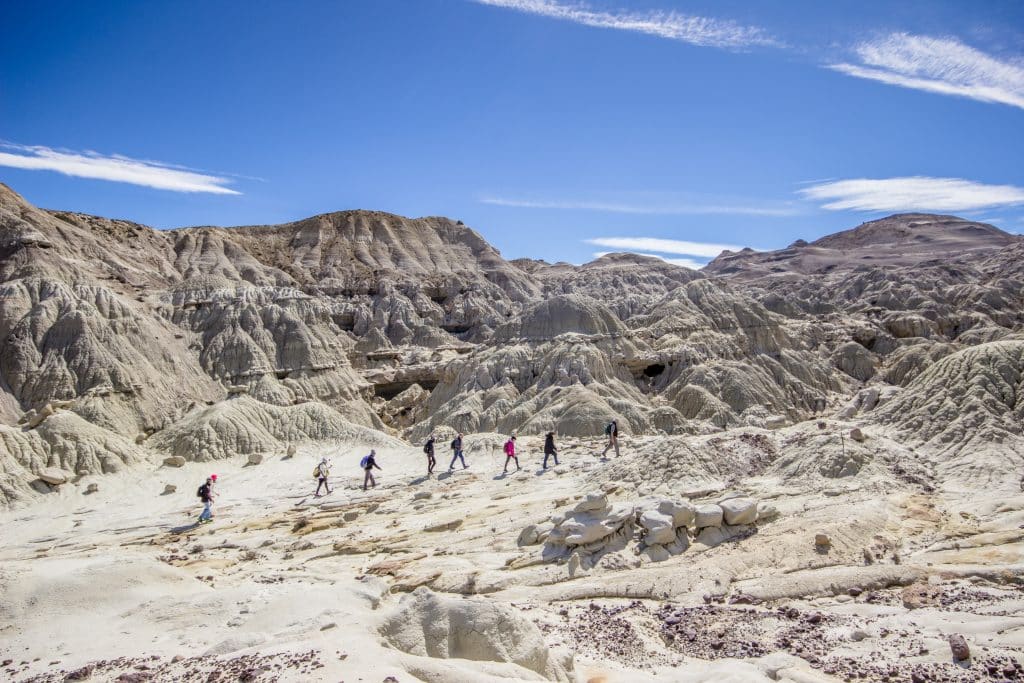 A line of hikers walking through a landscape that looks like the surface of the moon, all brown and rounded rocky surface.