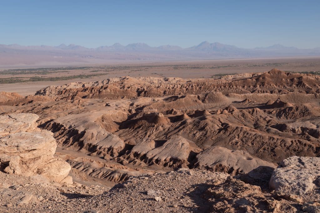 Looking into a valley of jagged, pointy, sand-colored rocks with faded blue mountains in the distance.