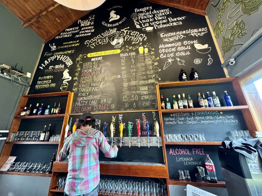 A bartender pouring beers at an enormous, tall bar, with lots of interesting craft beers written out on it.