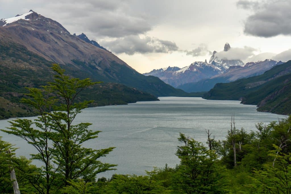 A still gray-blue lake surrounded by forests and mountains.