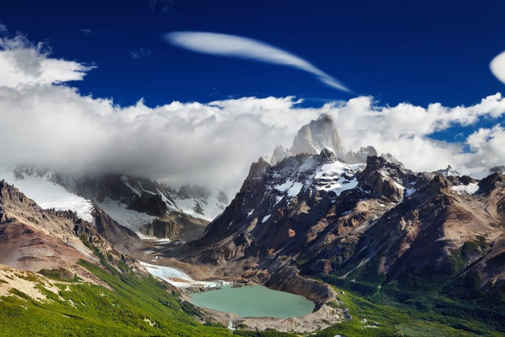 A small gray-green lake surrounded by jagged gray mountains with a low-hanging cloud dwarfing them.