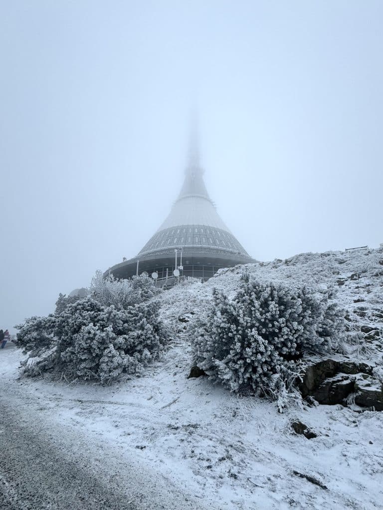 A tall pointy tower shaped like a spaceship, covered with snow and surrounded by fog.