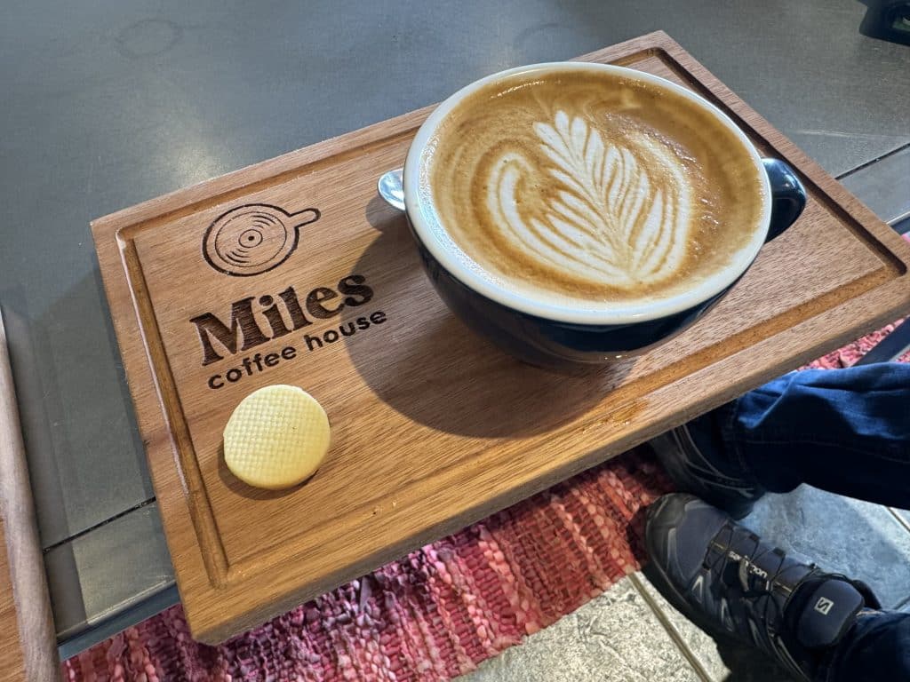 A perfectly pretty feathered latte on a wooden board reading Miles Coffee House.