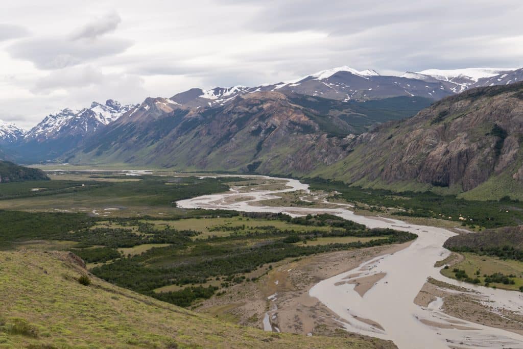 A river winding through a valley in Patagonia, tall snowcapped mountains on each side.