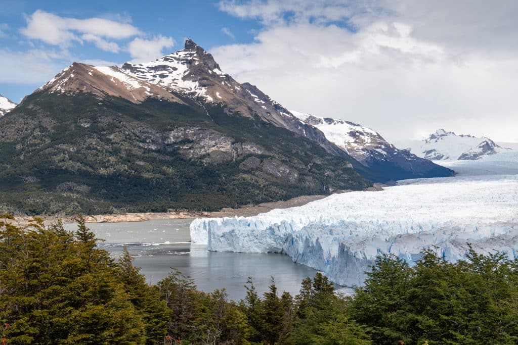 Big Perito Moreno Glacier resting on a lake, with a large, pointy gray mountain behind it.