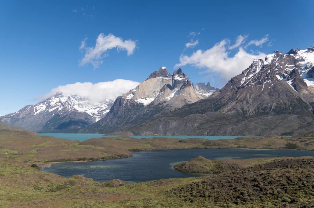 Bright turquoise lakes in front of snow-covered jagged gray mountains.