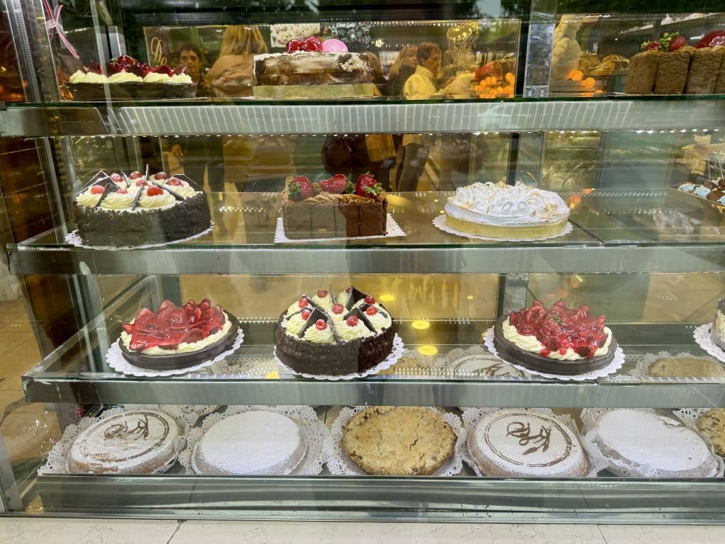 A window of a bakery with shelves covered in luscious-looking cakes.