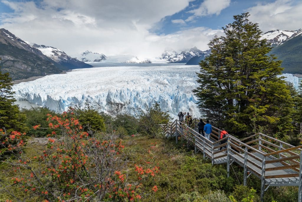 A walkway of stairs leading down to an enormous blue and white glacier surrounded by mountains.