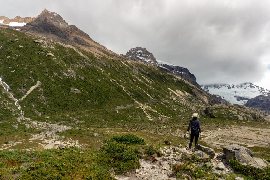 A hiker standing on a lookout in front of some jagged green mountains.