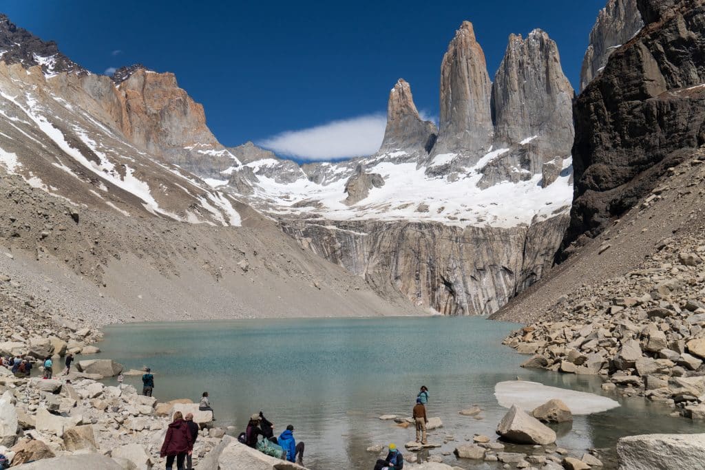 The first glimpse of the towers base, with hikers hanging around a pale turquoise lake with the three tall jagged gray towers behind them.