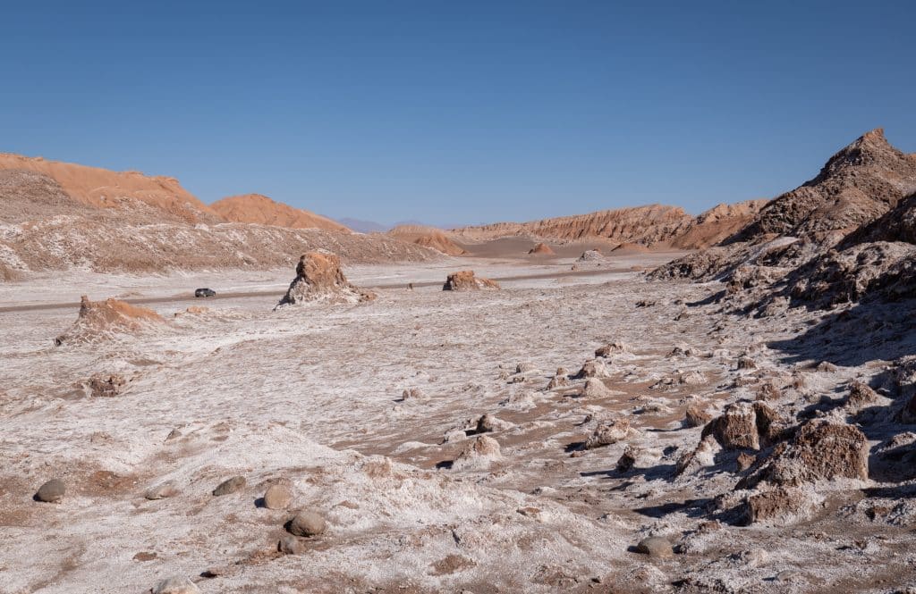 A pink, barren desert landscape, with lots of rocks and salty white streaks along the ground.