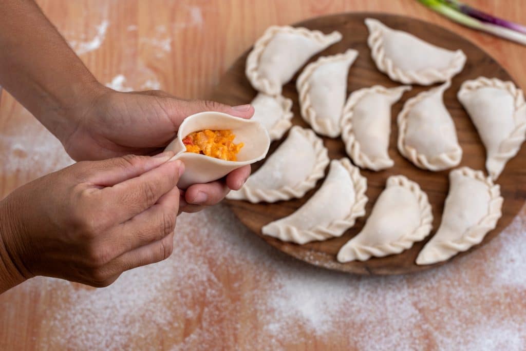 Hands folding dough into empanadas.