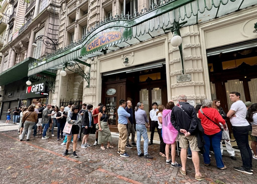 People standing in line outside Cafe Tortoni, with an Italian red, white and green sign.