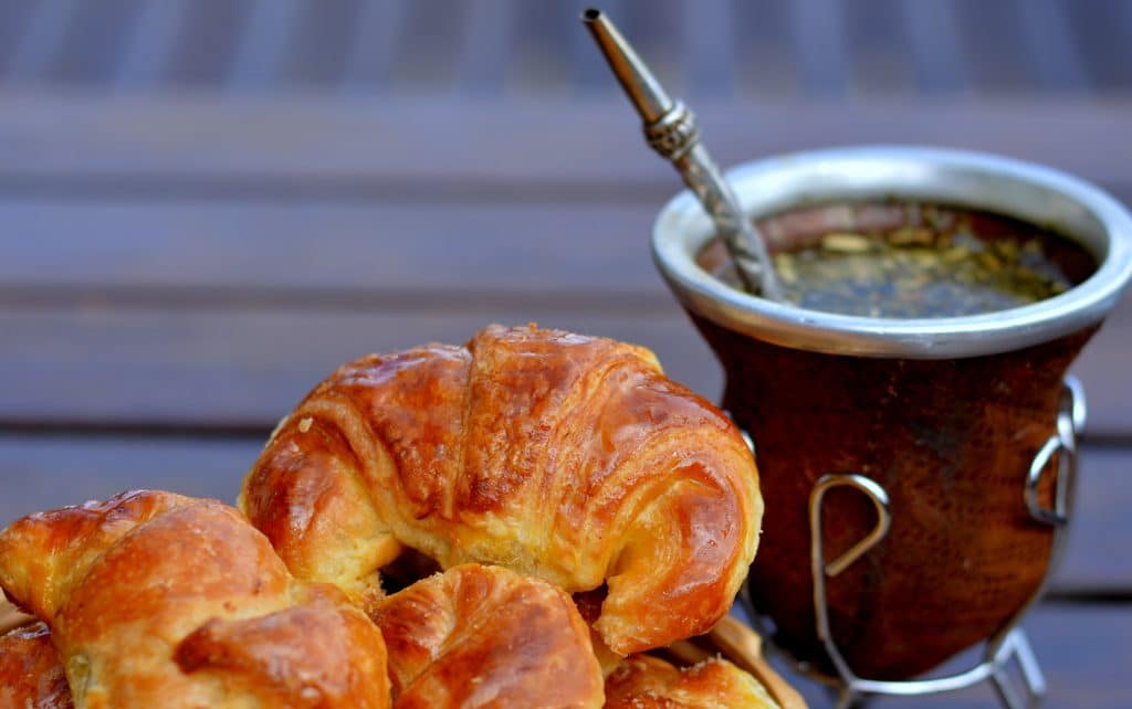 A small gourd-shaped container with a metal straw next to some croissants.