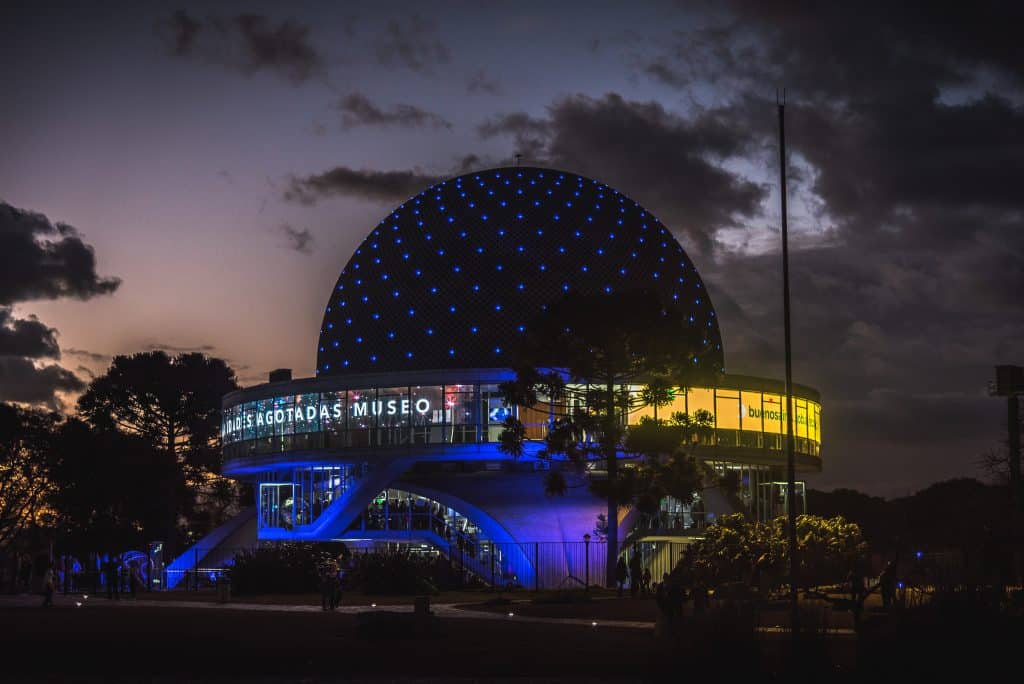 The round dome of a planetarium in front of a dark sunset sky.