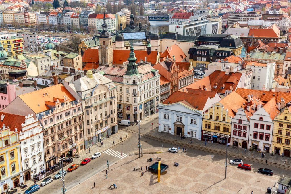 An overhead view of the colorful city of Plzen, with lots of buildings in warm shades of yellow, white, and pink.