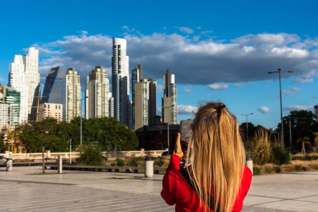 A woman photographing a neighborhood full of shiny skyscrapers.