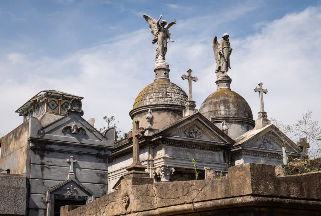Recoleta Cemetery in Argentina, with mausoleums topped with angels against the blue cloud-streaked sky.