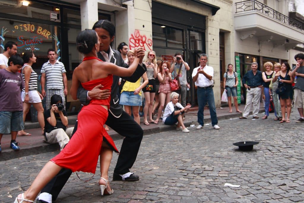 A man and woman tango dancing in front of a crowd on a cobblestone street.