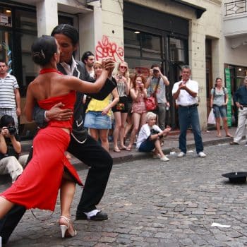 A man and woman tango dancing in front of a crowd on a cobblestone street.