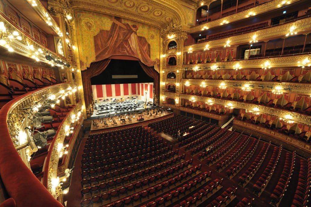 An immense theater with red velvet seats and lots of shimmering lights along the balconies.