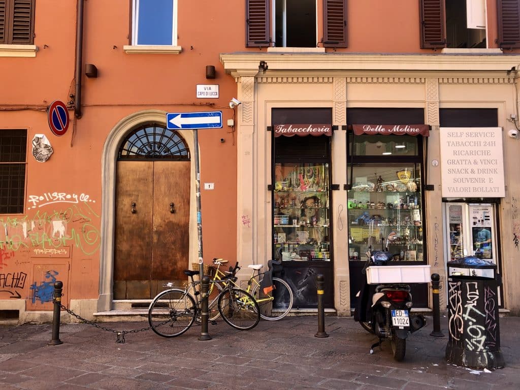 A street in Bologna with bikes parked in front of a residential door, next door to a small wine bar.