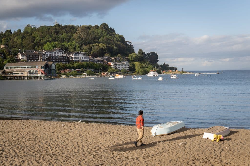 A boy standing on a sandy beach in front of a lake.