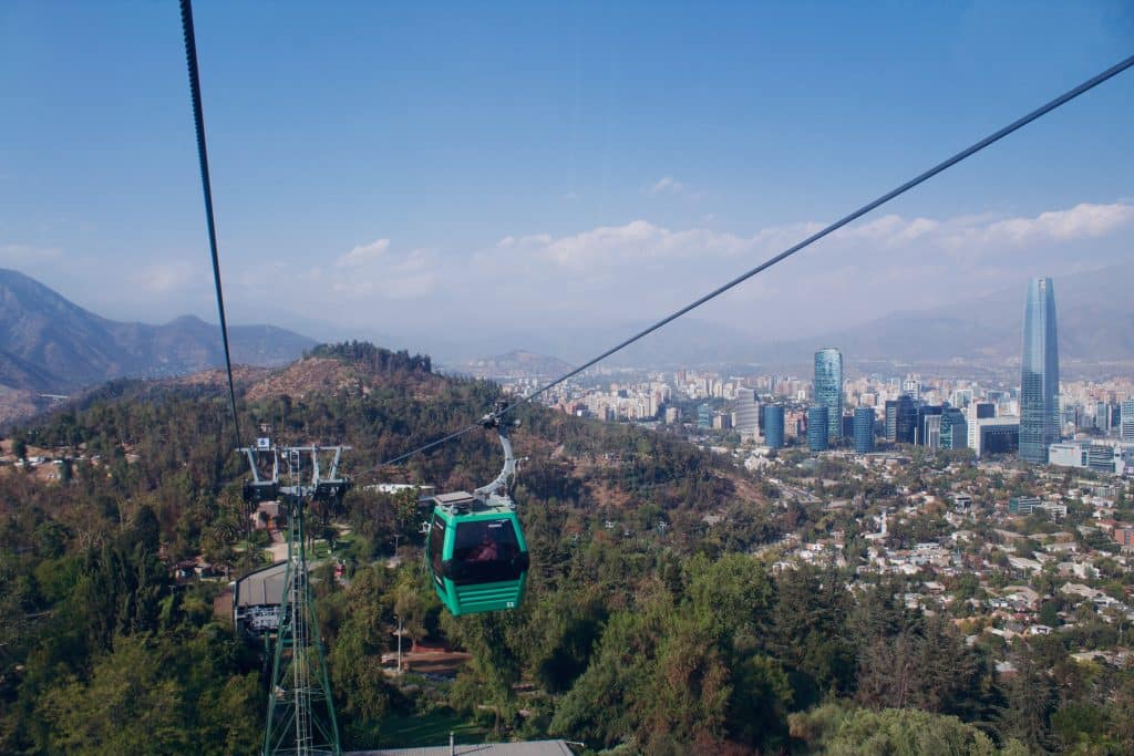 A cable car ascending a wire, the Santiago skyline and hills in the background.