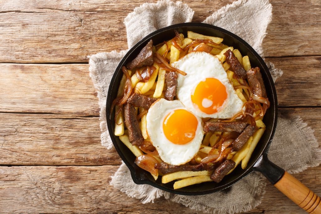 A skillet filled with French fries and meat, topped with two fried eggs.