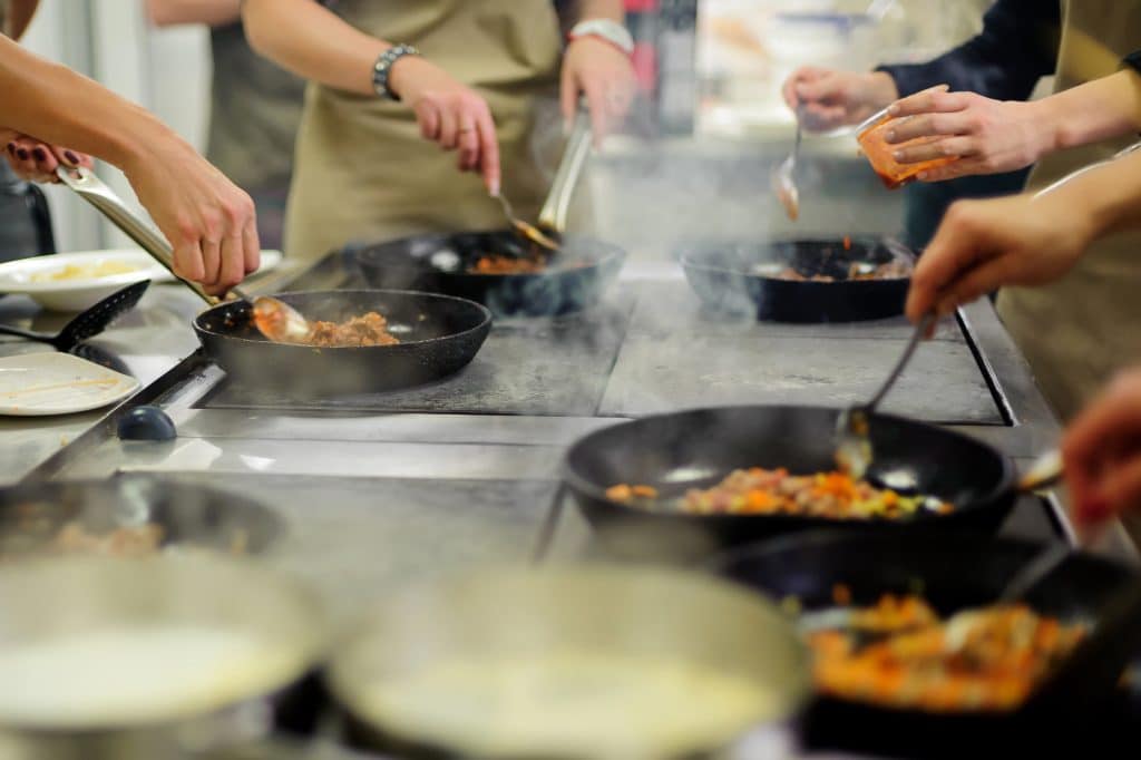 Several people cooking together in a class, all handling skillets on burners.