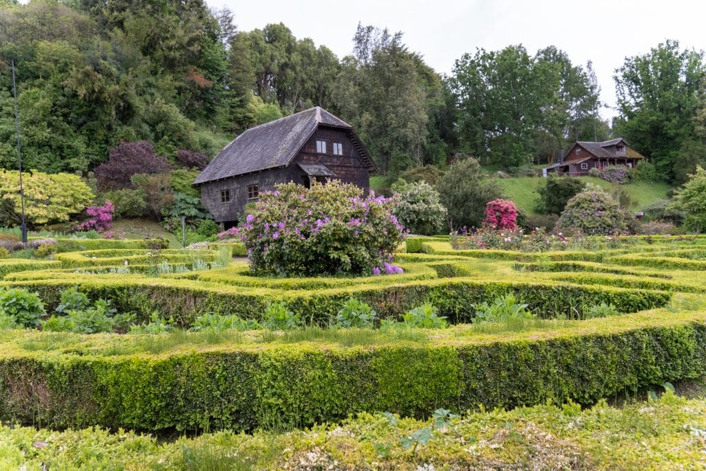 An old-fashioned German-looking timber house surrounded by lush gardens with shrubbery.