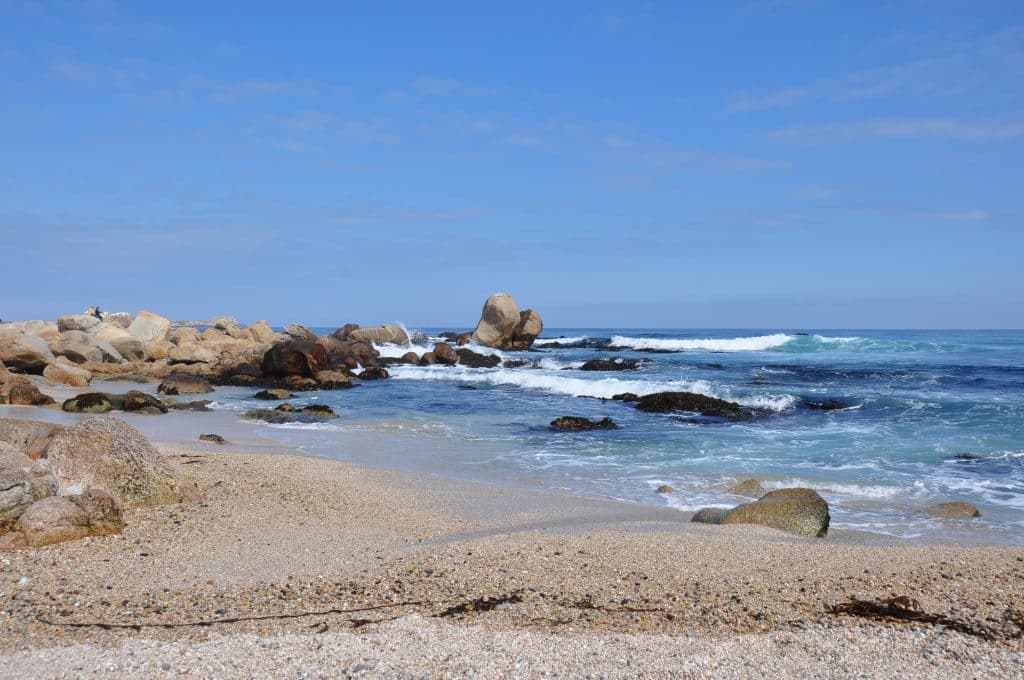 A sandy beach with lots of boulders on the beach and in the water.