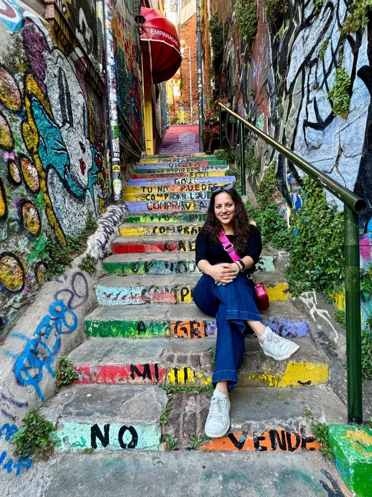 Kate sitting on a brightly painted staircase in Valparaiso, a smile on her face.