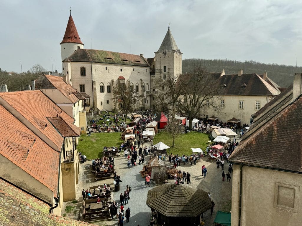 A Czech castle in the background, and in the foreground is a courtyard covered with stands at an Easter Market.