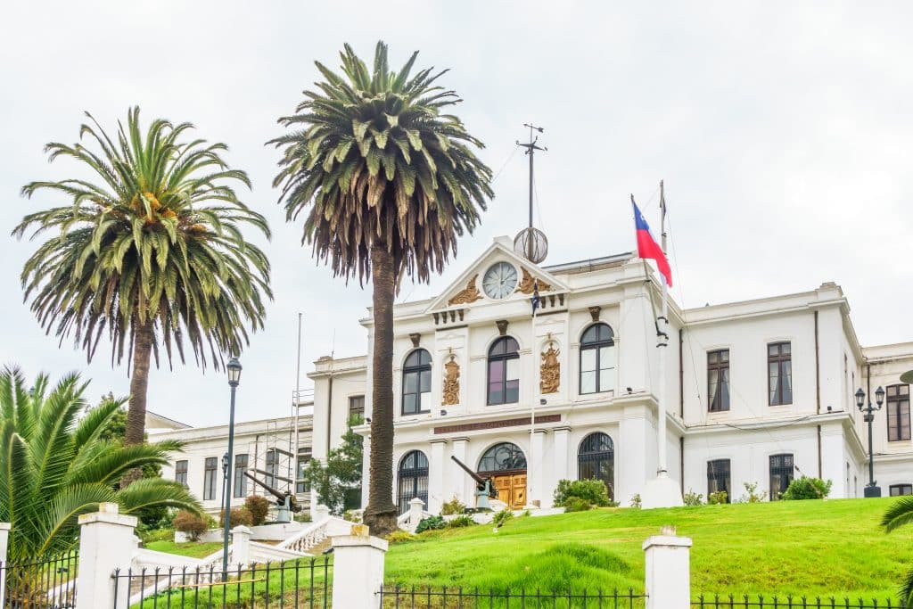 A big white colonial building with a Chilean flag and giant palm trees in front.