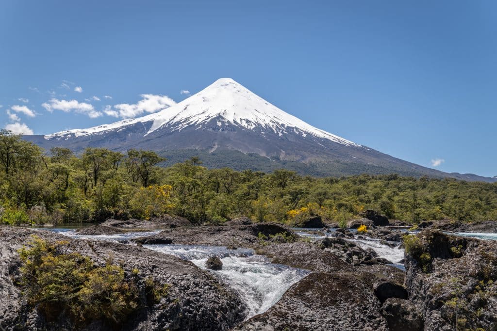 A tall, snow-capped conical volcano against a bright blue sky.