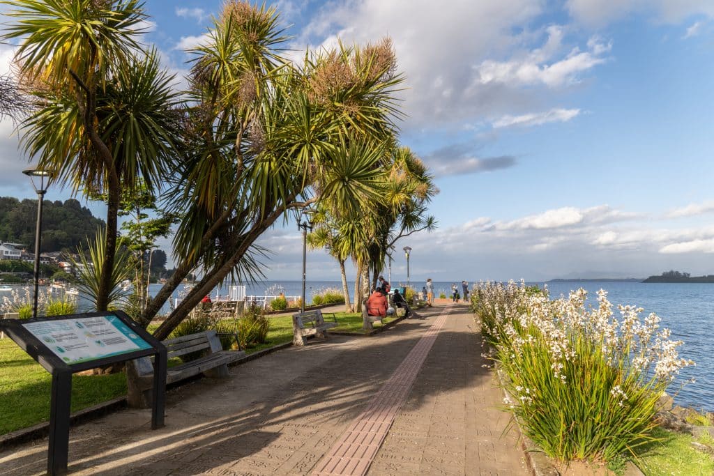 A tree and flower-filled park on a pier leading out to a bright blue lake.