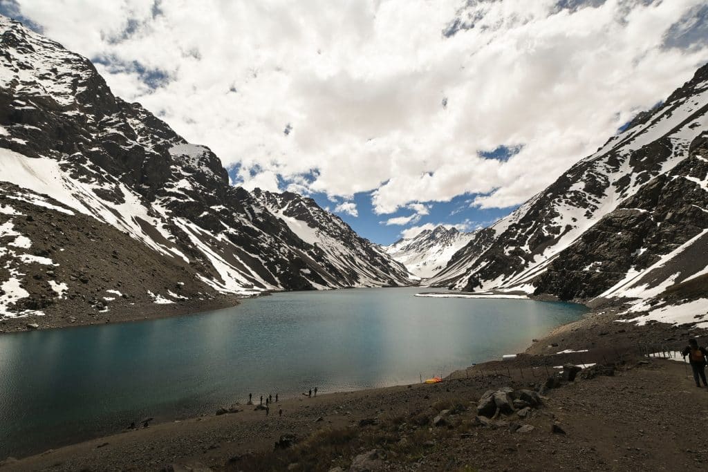 A pale blue lake surrounded by dark, snow-streaked mountains.