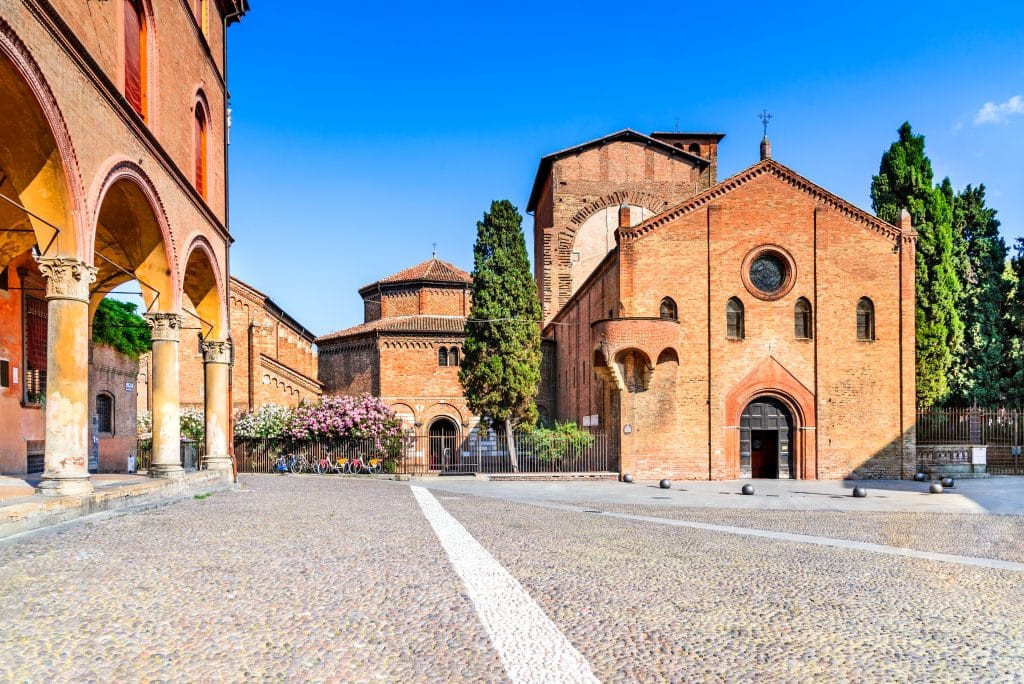 A short, red-colored church with cypress trees on each side.