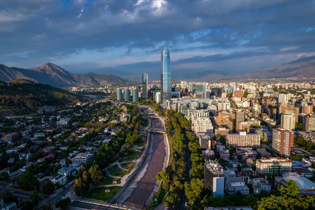 An aerial view of Santiago Chile, with the tall, teal Sky Costanera building dominating the skyline.