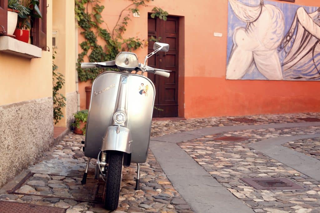 A silver vespa parked on a cobblestone street in Bologna.