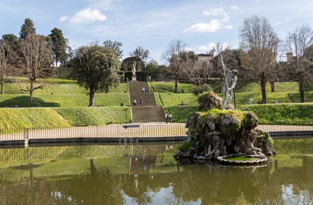 Big landscaped green gardens in Florence, with a marble statue on an island in a pond, and a big staircase leading up the hill.