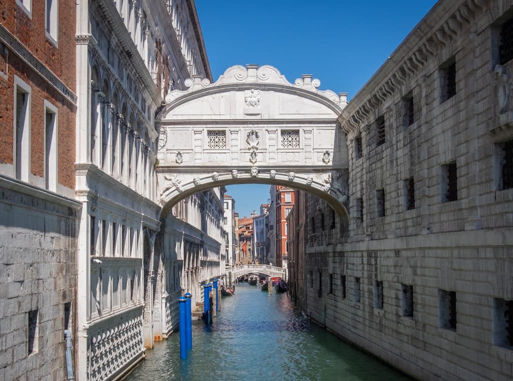 An elegant carved white bridge connecting two buildings on either side of a canal in Venice.