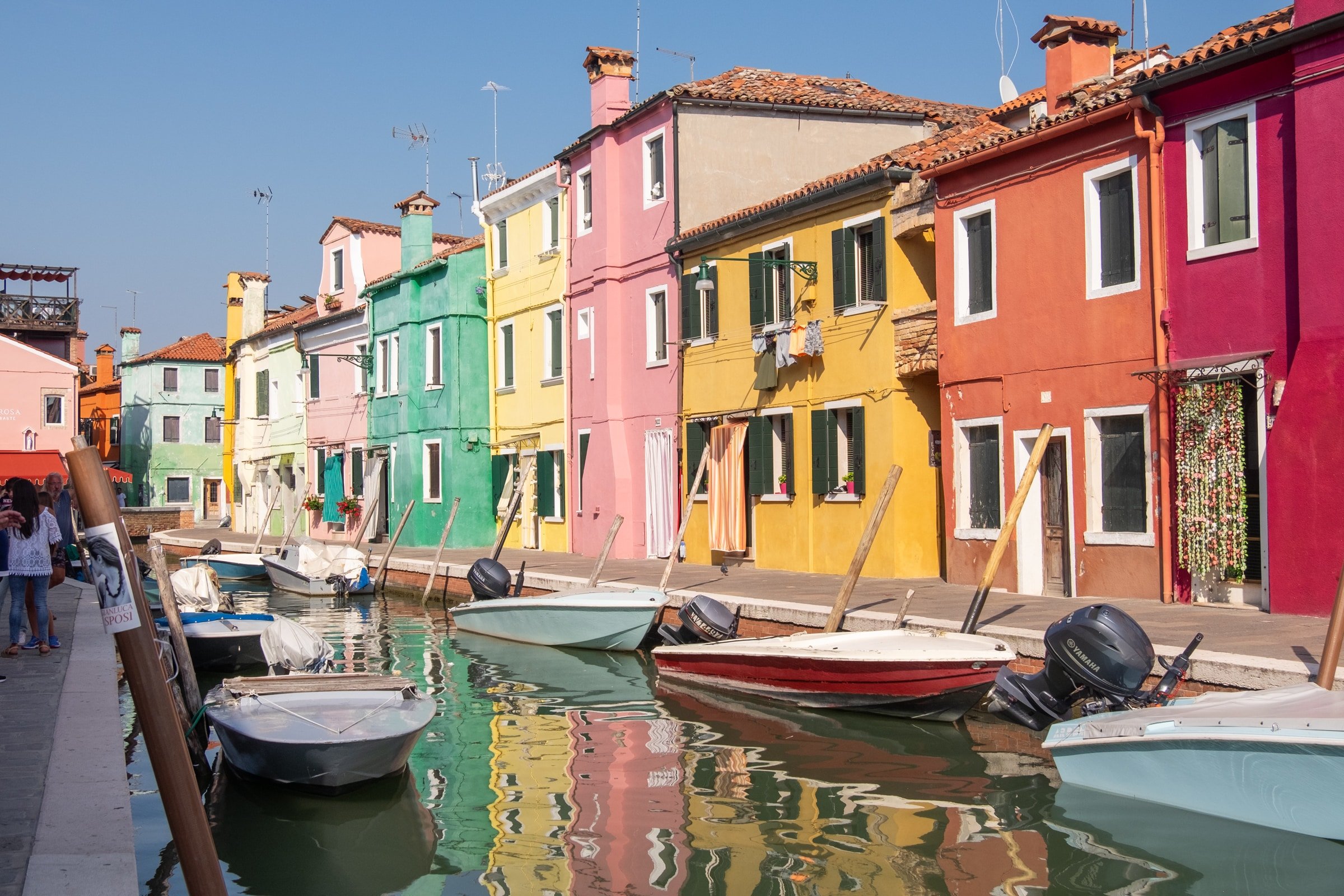 Colorful houses lining a canal in Burano, Italy, a small island near Venice, with a bridge and small boats.