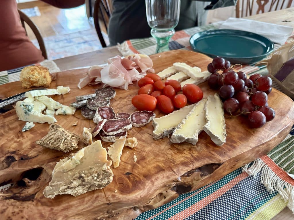 A charcuterie board topped with lots of French cheeses, plus grapes and tomatoes